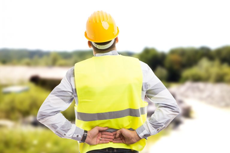 Injured construction worker or engineer suffering backpain in lower back area outdoor at work